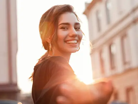 A young woman smiling over her shoulder on a city street in warm evening light