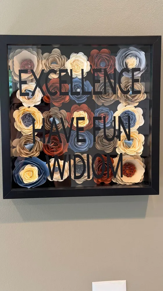 Shadow box of paper flowers spelling out Excellence, Have Fun, and WIDIOM on the office wall