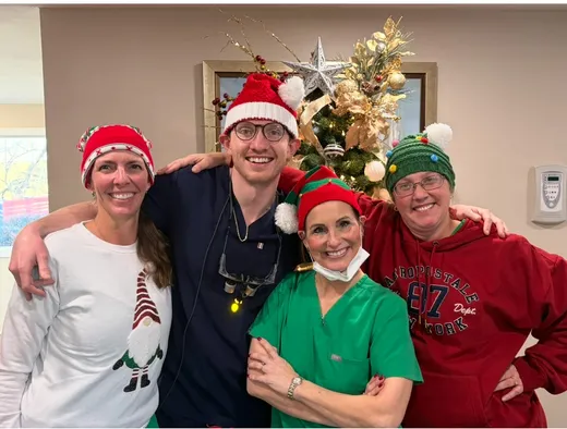 Four team members in Christmas hats in front of the office tree