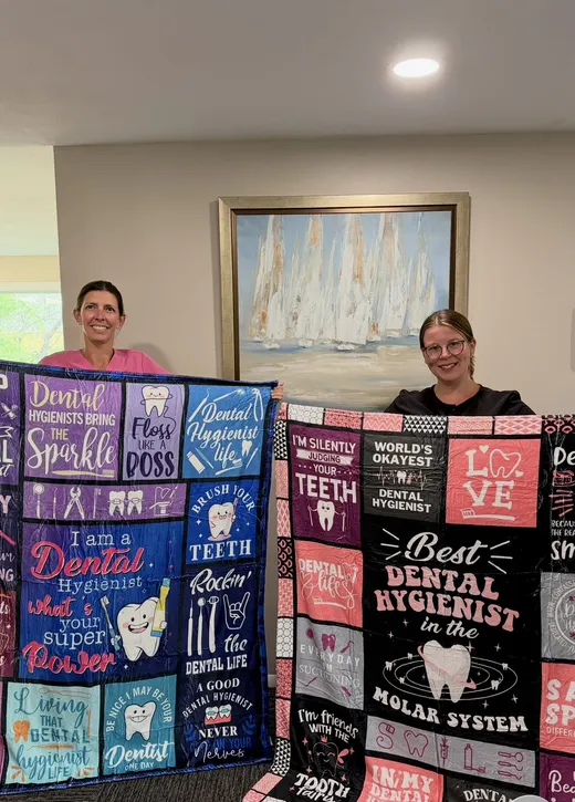 Two hygienists holding dental hygienist themed blankets in the office